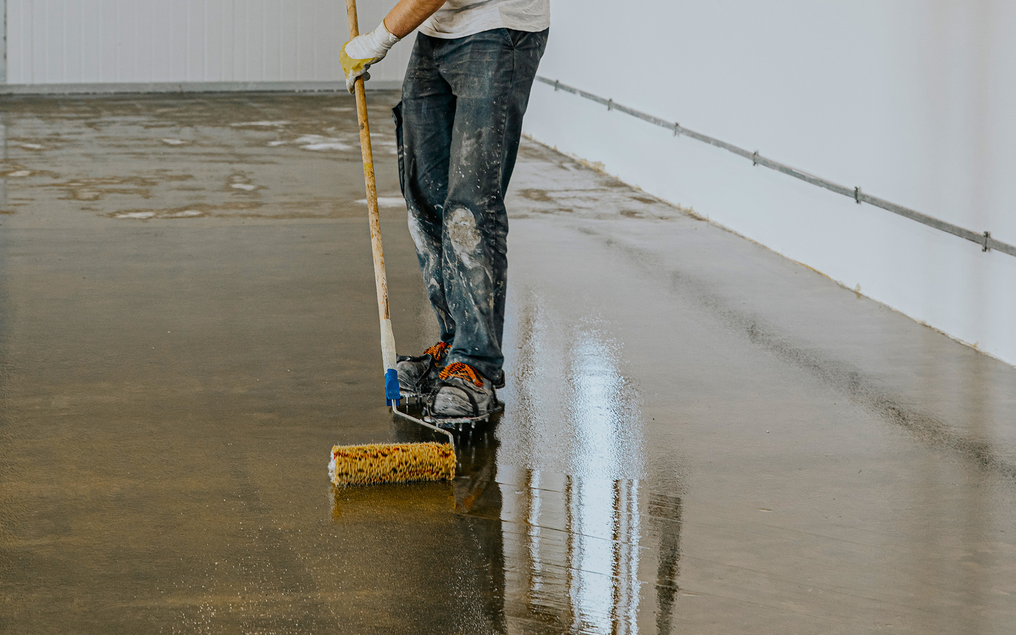 Worker, coating floor with self-leveling epoxy resin in industrial workshop